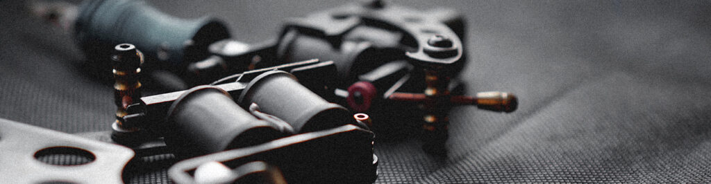 Tattoo machine and tattoo supplies on dark background - for banners